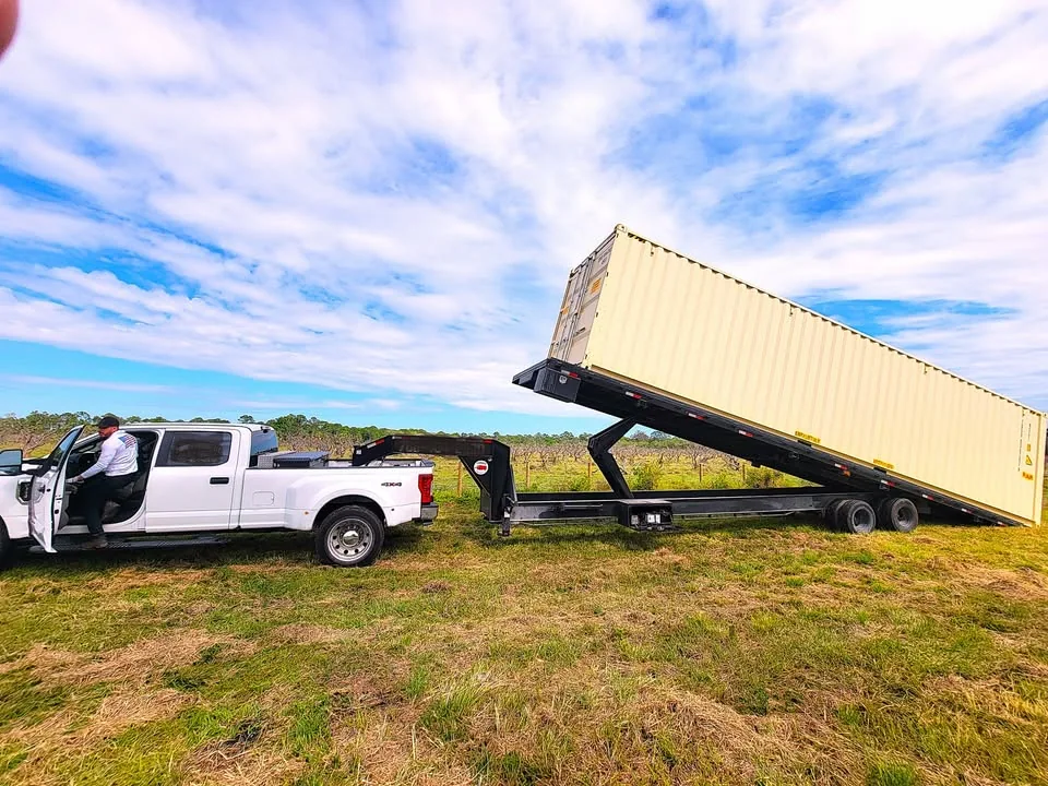 White shipping container being unloaded from a tilted delivery trailer.