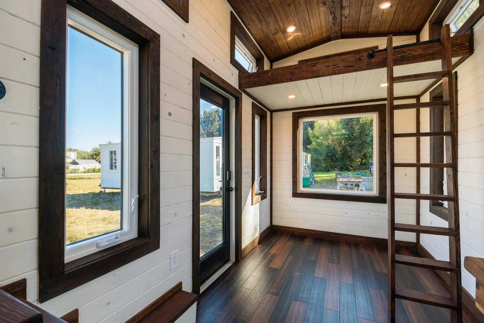 Bright tiny house interior with large windows and loft access.